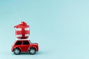 Red toy model car with gift box on blue background. Christmas and New year delivery concept photo