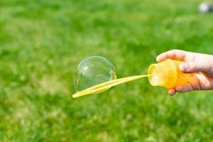 childs hand holding a wand for blowing soap bubbles against green grass in a sunny summer day. photo