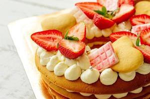 Sponge cake with strawberries, pink milk chocolate bars, silver sprinkles, vanilla cream and heart chape cookies close up. Summer sweet dessert for birthday or mothers day photo