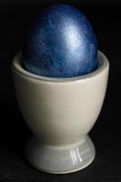 Dark blue Easter egg in ceramic holder on black background. Concept of minimal festive Easter backdrop photo