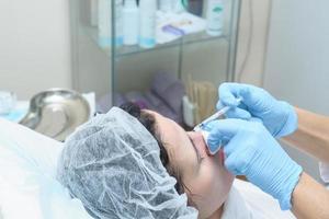 hands of cosmetologist in blue latex gloves making botox injection in female face. photo