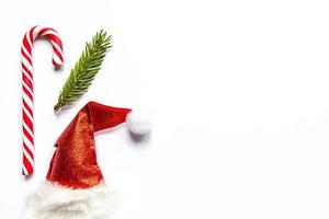 santa hat and candy cane and fir tree branch on white background. Creative new year flat lay with copy space. Minimalistic style photo