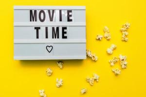 Movie Time text on a light box. Scattered salty popconn on yellow background photo