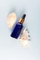Dropper blue glass cosmetic bottle mock up and seashells on blue background. Eco friendly care organic product for skin care. Beauty treatment, spa concept. Copy space photo