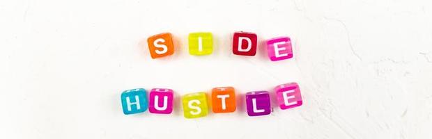 Side hustle phrase made of cube beads of different colors on white concrete background. Conxep of additional income. photo