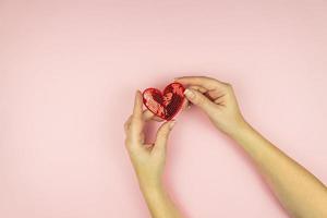 Female hands holding red sequin heart on pink background. Creative minimal layout with copy space photo