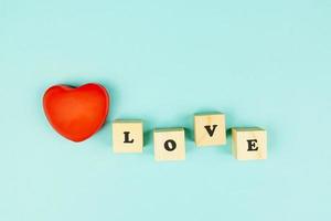 Red heart and wooden cubes with text LOVE on blue background. Creative flat lay with copy space. Festive greeting card for St Valentines day. photo