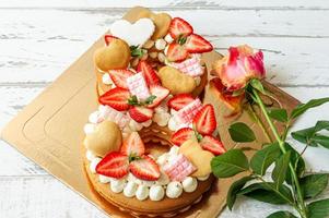 bizcocho con fresas, barras de chocolate rosa, crema de vainilla y galletas de corazón en forma de número 8 con rosa rosa. un regalo especial para el día internacional de la mujer. dulce regalo foto