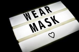 signo de caja de luz con máscara de uso de cita sobre fondo negro. medidas de protección contra el coronavirus. foto