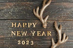 feliz año nuevo 2023. cita hecha de letras de madera y números 2023 sobre fondo de madera decorado con cuernos de ciervo. concepto creativo para la tarjeta de felicitación de año nuevo foto