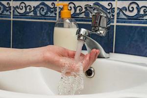 Female hands under running water from bathroom sink faucet. Hygiene concept photo