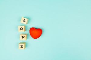 Red heart and wooden cubes with text LOVE on blue background. Creative flat lay with copy space. Festive greeting card for St Valentines day. photo