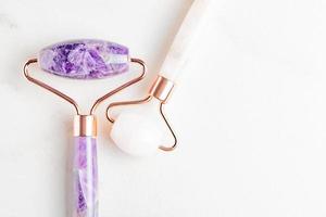 Amethyst and rose quartz massage rollers on marble background. Pink jade stone for face and body care. Horizontal shoot. Flat lay, top view. Copy space for your text photo