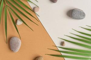 Zen flat lay composition with green leafs and stones. Tropical leaf and sea pebble on beige background. Spa or beauty template with place for text or product . Blank card with tropical leaves. photo
