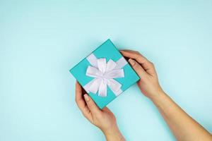 Woman holding blue gift box on color blue background. Festive greeting card. Holiday concept photo