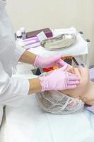 Beautician in pink gloves applies peeling on woman face. Cosmetic procedure for rejuvenation and cleansing of the skin. Spa treatment photo