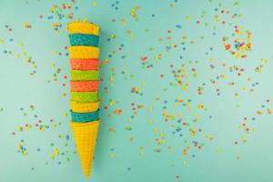 Set of various bright multicolored ice-cream waffle cones on blue background with scattered confetti sugar sprinkles. photo