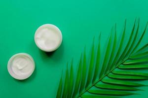 tarro blanco de crema facial sobre un fondo de hoja verde palmera tropical. fondo verde, vista superior, endecha plana. concepto de cosmética natural. foto
