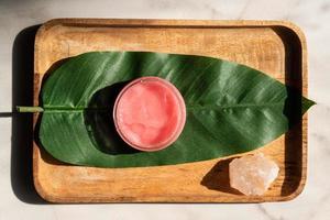 Pink strawberry scrub or cream and green leaves on wooden background. Skin care beauty and spa concept. photo