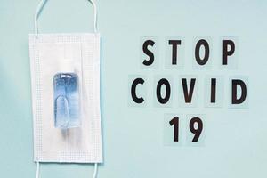 medical mask and sanitizer on blue background and text stop covid 19. hygienic quarantine concept. Flat lay, top view photo