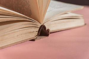 Open hardcover old book on pink background with copy space. Educational concept photo