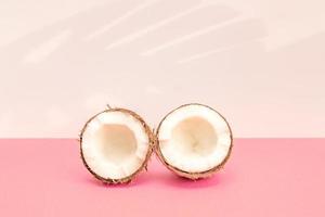 Two halves of fresh raw coconut on pink backgound with kight shadows in white. photo