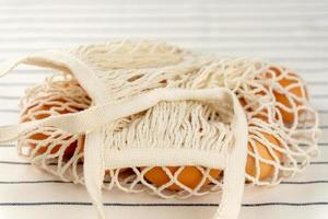 Easter concept. No plastic bag concept. Minimal style. Beige mesh shopping bag with brown chicken eggs on textile background. photo