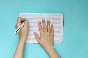 Left handed woman makes notes in her planning or dary on blue background. Planning concept. Flat lay style. photo