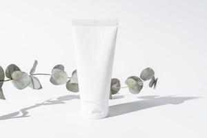 loción de crema de belleza blanca cosmético de protección solar spf en envases de tubo. maqueta de producto con rama de eucalipto a la luz del sol. cuidado de la piel facial, cuidado de la salud foto