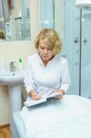 middle aged woman in white coat making notes in blue daily planner. Doctor female, medical professional photo