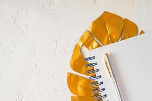 Stylish mock up composition with gold monstera leaf, empty notebook and a pen. Copy space for text photo