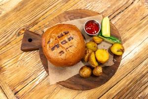 Burger with meat served with cucumbers, cetchup and fried baby potato on round cutting board. Unhealty dinner photo