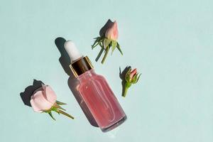 Transparent glass cosmetic bottle with a dropper on a blue background. Natural cosmetics concept, natural essential rose oil and skin care products photo