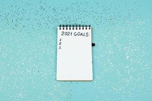 Small notebook on blue confetti background with written 2021 goals for new year. Resolutions list. photo