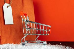 concepto de amante de las compras: bolsas de compras de papel rojo y carrito de compras de juguete pequeño sobre fondo rojo foto