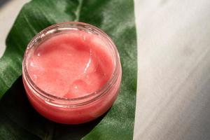 natural herbal cosmetic product for skin care. face and body jelly scrub in glass jar on green leaf photo