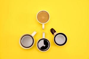 un montón de tazas de café con diferentes tazas de café sobre fondo amarillo. concepto de moda, vista superior foto