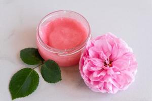 Hygiene bath product. Body, face rose scrub with blooming pink rose flowers on marble background. Wellness therapy regeneration and skin care concept photo