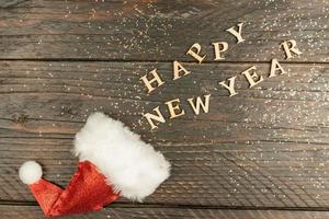 festive greeting card for new year with red santa hat and wooden text scettered out of it on a table. copy psace for text photo