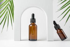 frascos cuentagotas de vidrio con una pipeta con punta de goma negra y hojas verdes cerca de ella sobre fondo blanco. concepto de piel natural. cosméticos de spa orgánicos. foto