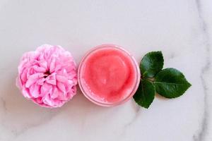 Hygiene bath product. Body, face rose scrub with blooming pink rose flowers on marble background. Wellness therapy regeneration and skin care concept photo