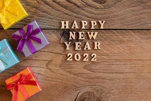 Multicolored gift boxs. New year presents on wooden table. Tex Happy new year 2022. Festive greeting card. Flat lay. photo