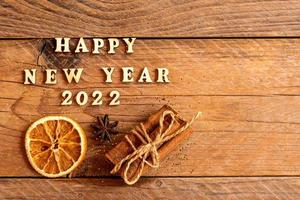 Cinnamon sticks, slices of dried orange, star anise and quote happy new year 2022 on wooden background with copy space. Top view. Christmas and New Year celebration concept. photo