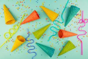 bright multicolored ice-cream waffle cones and cocktail straws on blue background with scattered confetti sugar sprinkles. photo