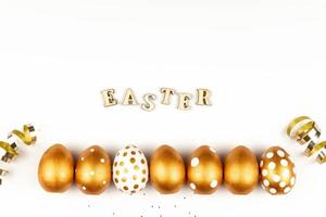 Easter festive decoration. Top view of easter eggs colored with golden paint and inscription in English Happy Easter. Wooden letters on white background. Various dotted design photo