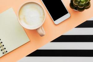 Modern white office desk table with smartphone and cup of coffee. Blank notebook page for input the text. Top view, flat lay. photo