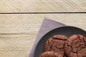 Top view of homemade chocoate cookies on black plate on wooden background. Home bakery photo