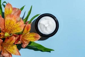 open cosmetic jars with nourishing or moisturizing cream on a blue background and alstroemeria flower with copy space photo