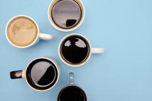 Many cups of different aromatic hot coffee on blue background, top view photo