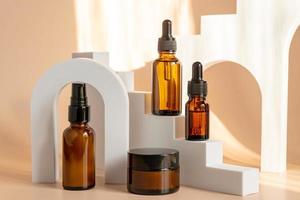 Beauty product concept. Jar of cream and bottles of serum on beige backgrounds. Front view. Trendy showcase with hard light photo